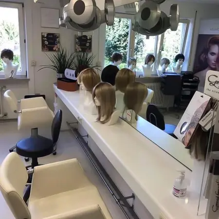 Heller Perückenladen mit Frisierstühlen, Spiegel und verschiedenen Damenperücken aufgestellt.