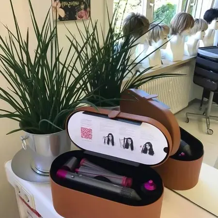 Stylinggerät im offenen Etui auf Frisiertisch, umgeben von Pflanzen und Perücken.